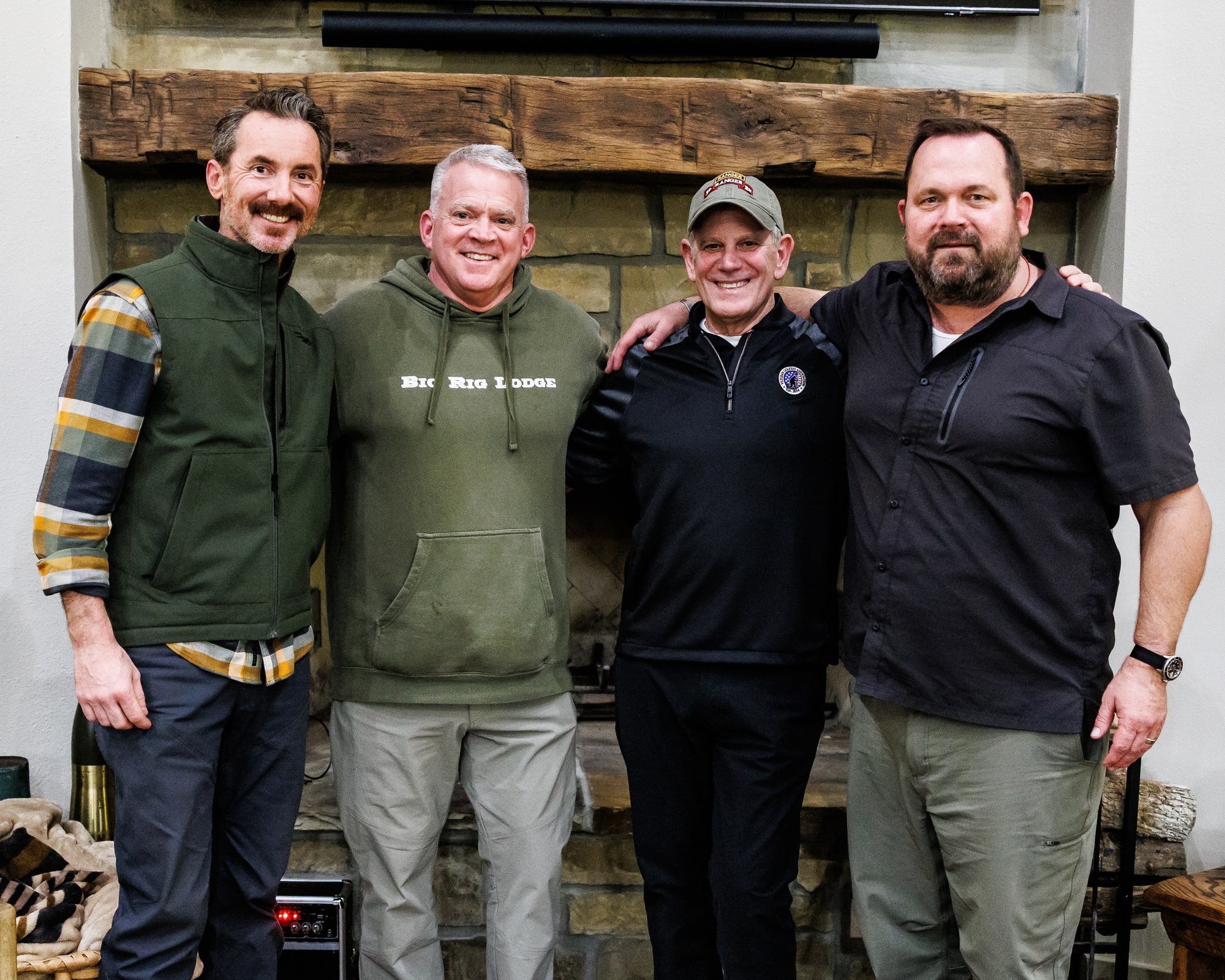 Four Darby's Warrior Support leaders standing together in front of the stone fireplace at the corporate retreat lodge